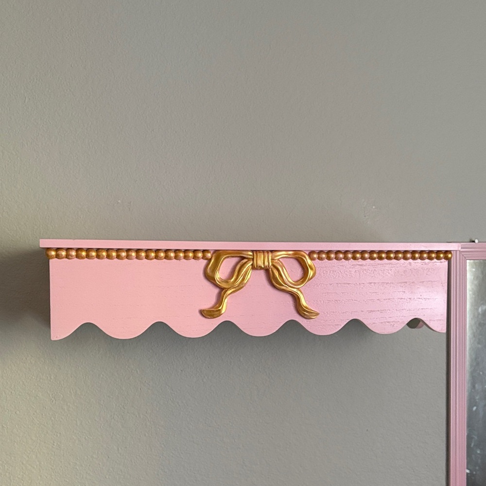 Pink wall shelf with gold bow accents and necklace rack